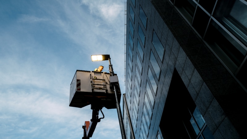 Worker maintaining outdoor LED lighting fixture for energy efficiency.